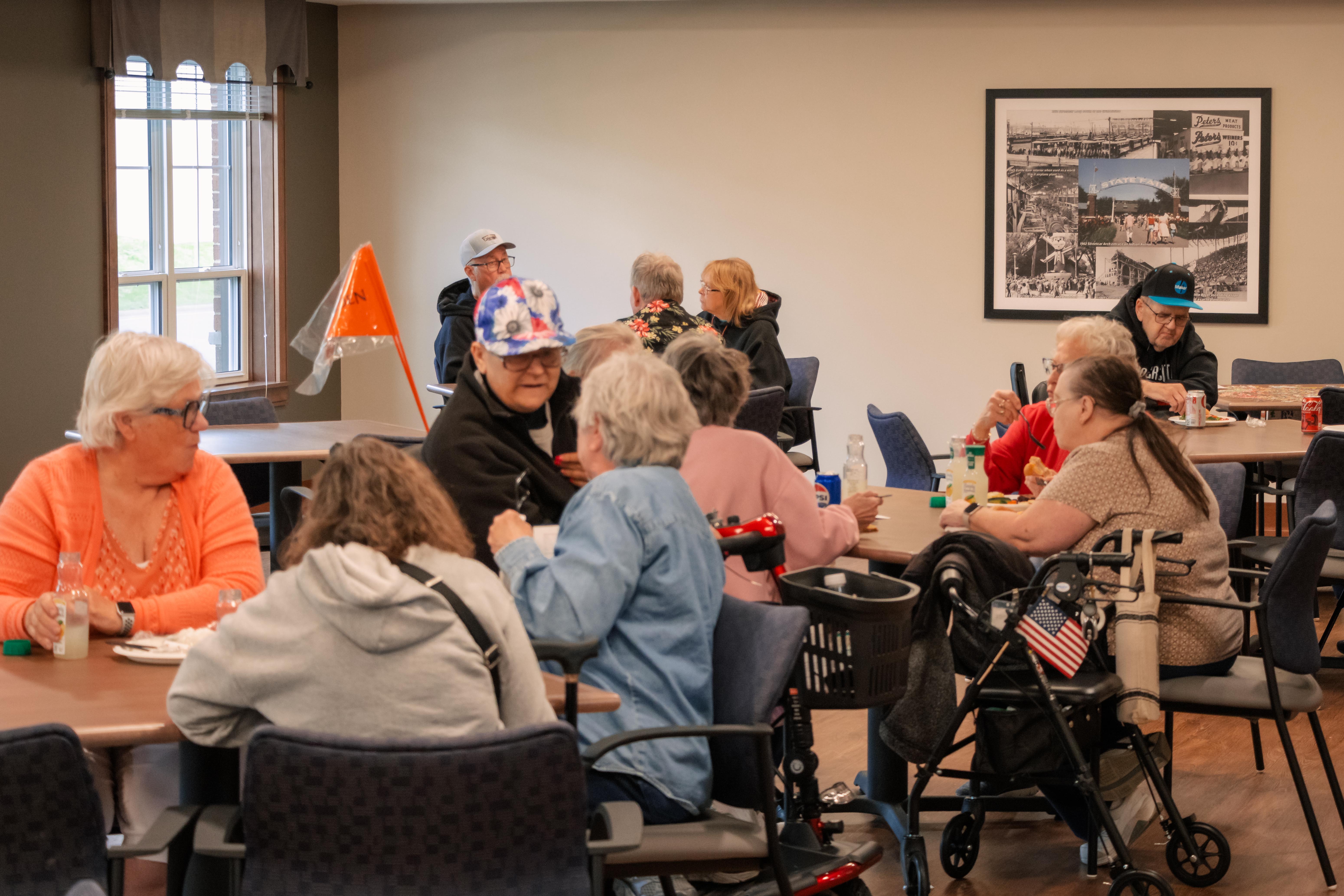 A room of older adults sitting at tables and sharing a meal in a community room