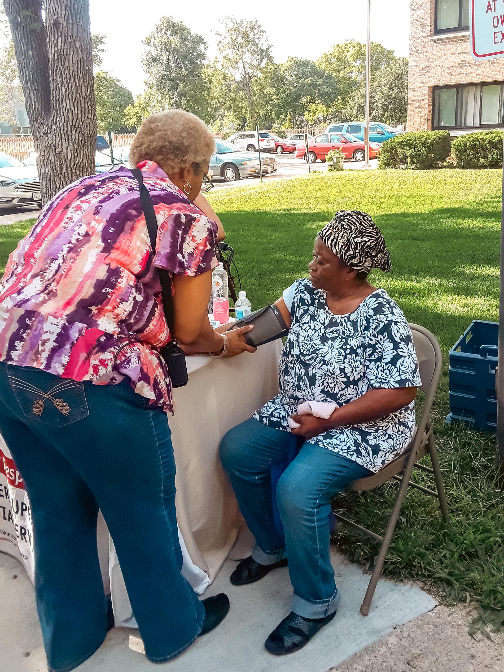 a woman checking the blood pressure of an older adult in an outdoor setting