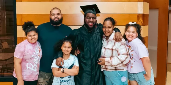 a diverse family posing with a young high school graduate in a black cap and gown