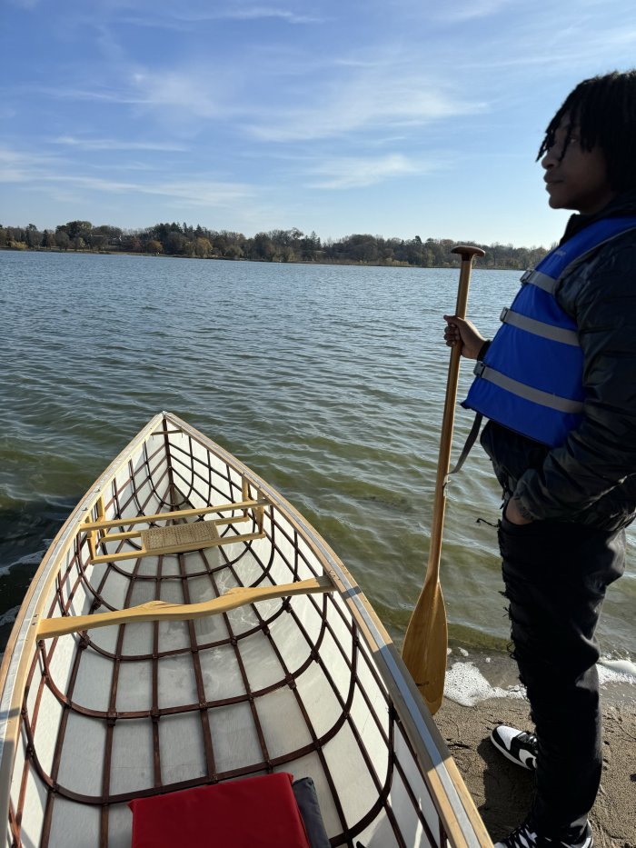 A student standing next to a canoe that is partially in the lake