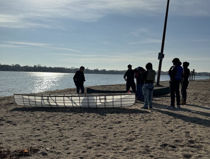 Students and staff standing near a canoe on a beach of a lake