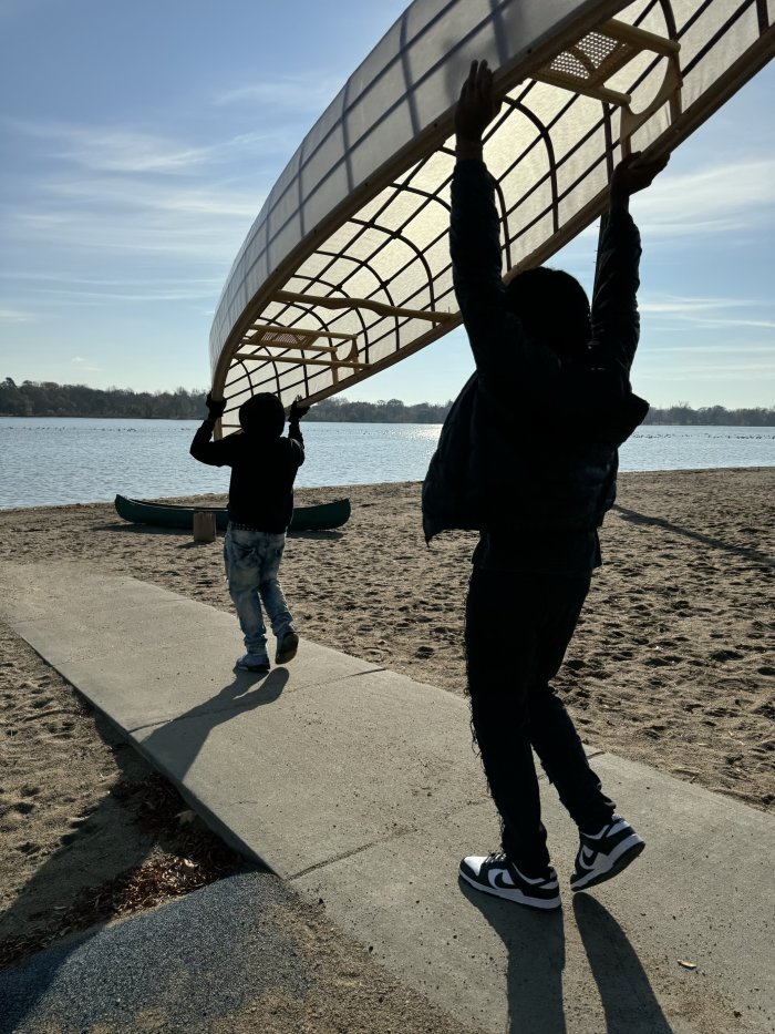 Two students silhouetted by the sun carrying a canoe above their heads