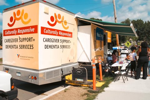 a mobile clinic parked on the street with community members visiting a table set up out in front