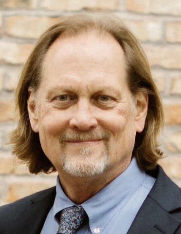 A headshot of a man in a suit grinning