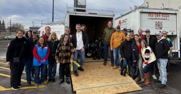 A group of people standing in front of a trailer filled with bicycles smiling in an outdoor setting