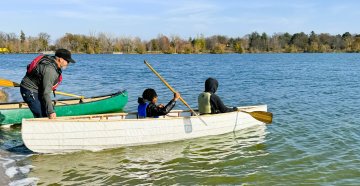 Two young adults are sitting in a canoe on a lake that is being held by an adult