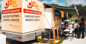 a mobile clinic parked on the street with community members visiting a table set up out in front