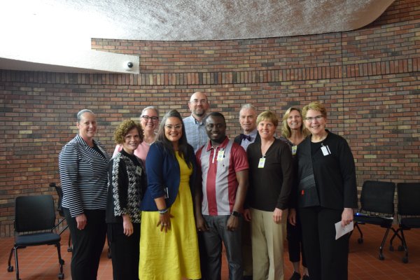 A group of diverse individuals standing together in front of a brick wall smiling at the camera