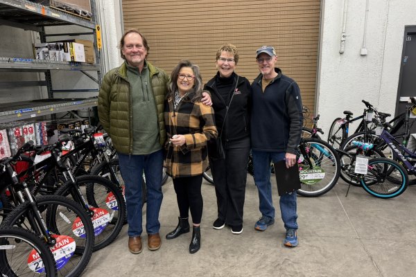 Four individuals standing and smiling in front of bikes lined up in a store backroom