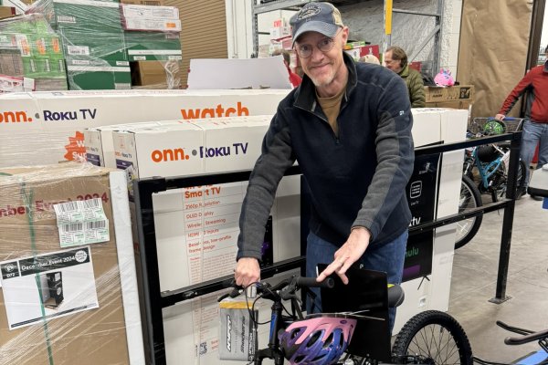 A man smiling and pushing a children's bike through a store backroom